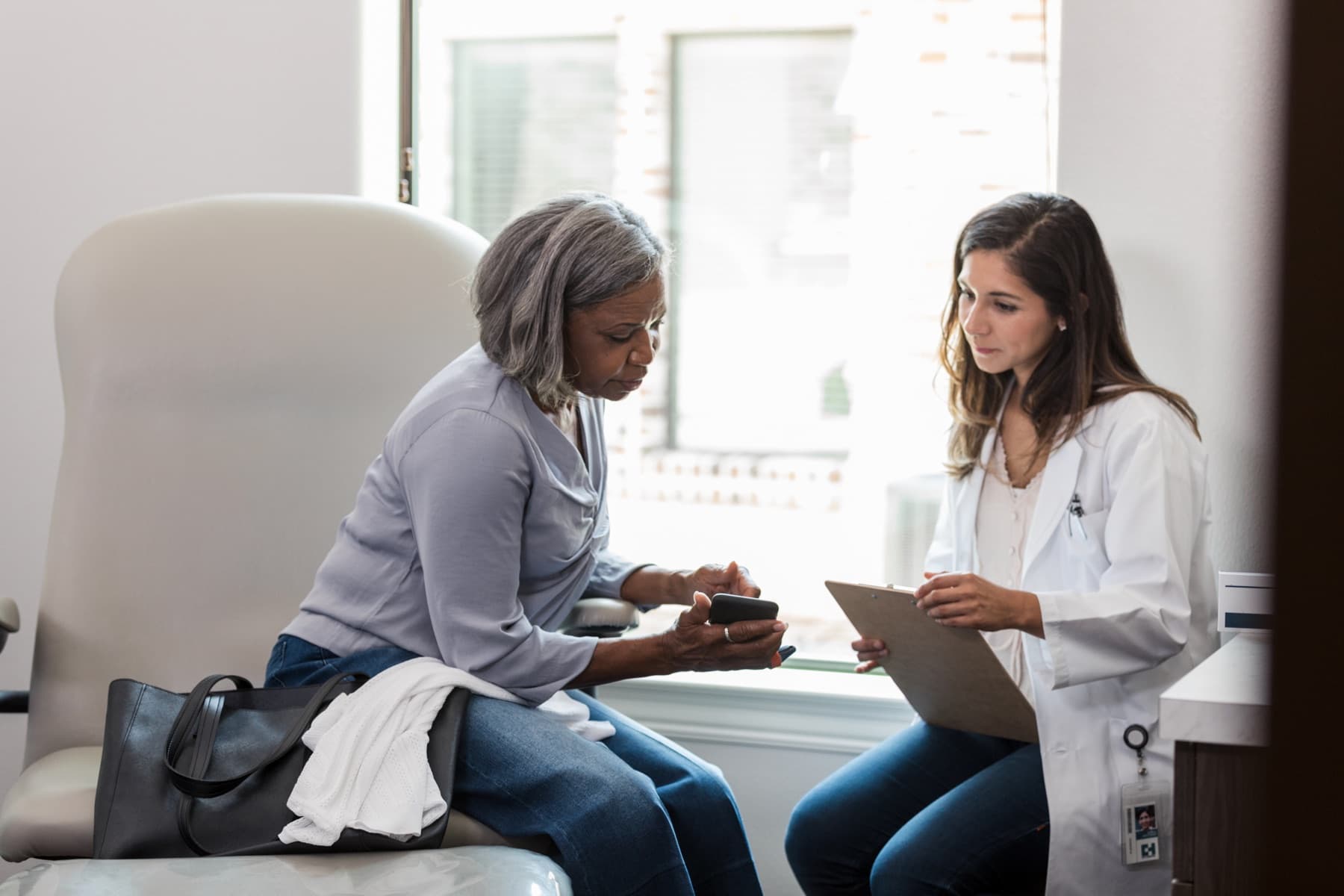 A woman showing her phone to her doctor across the exam table.