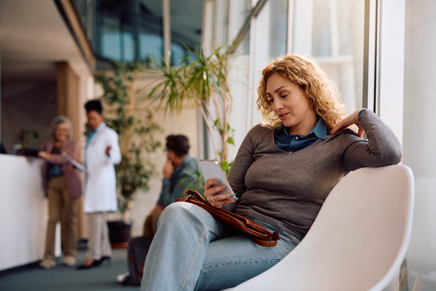 A woman in a clinic waiting room, preparing on her phone before her appointment.