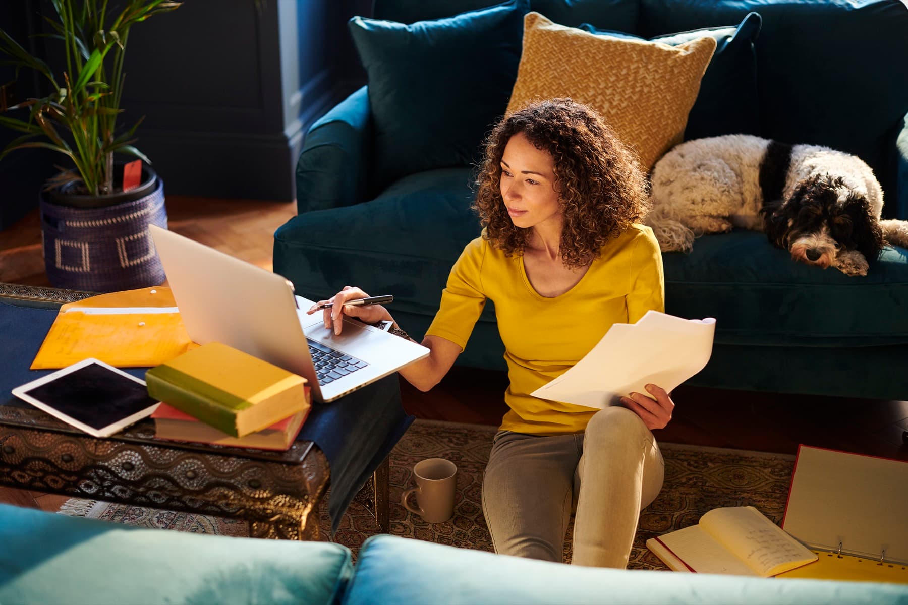 A woman at home with a laptop, notebook, and tablet, keeping track of her own health.